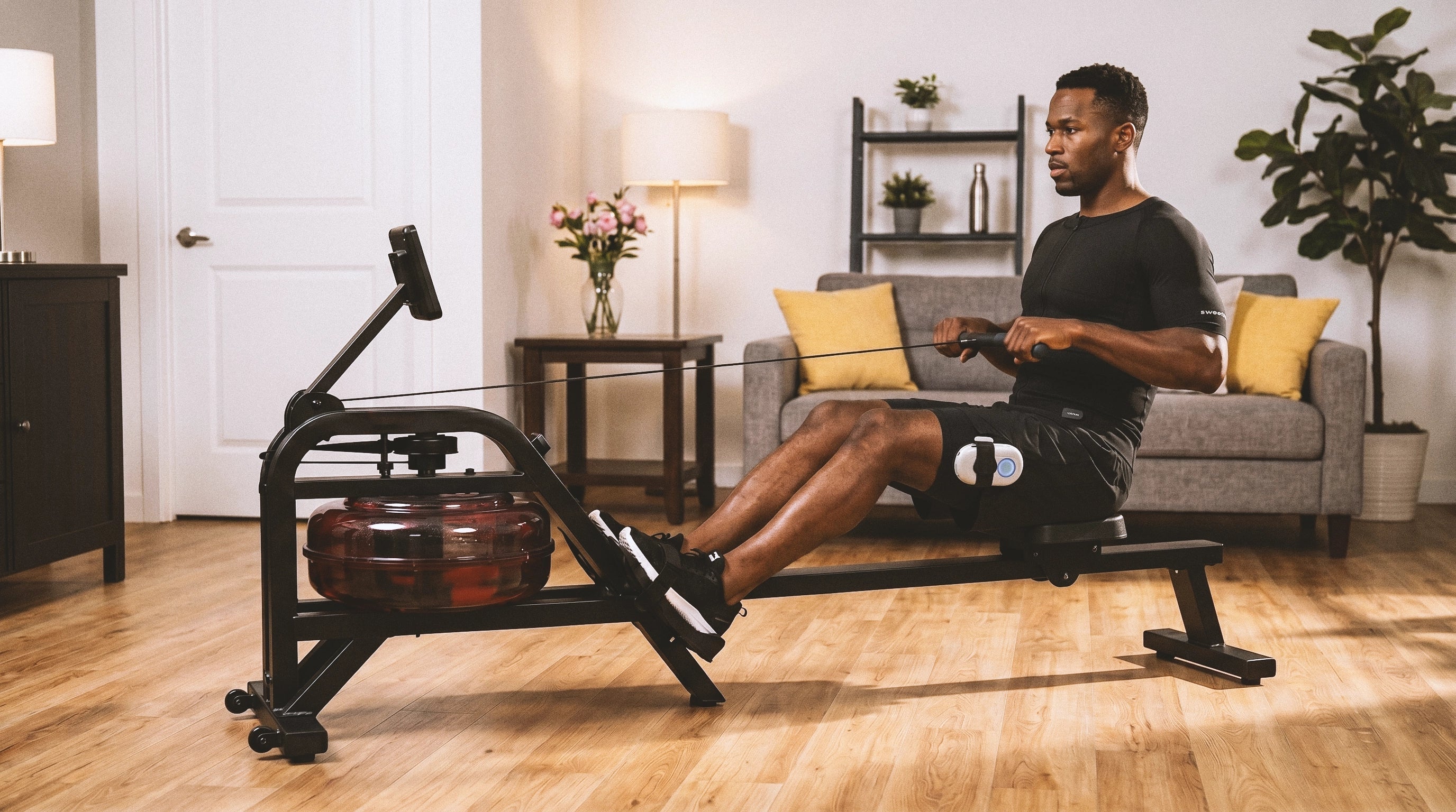 Man wearing EMS training gear uses a rowing machine at home for safe low impact muscle stimulation exercise