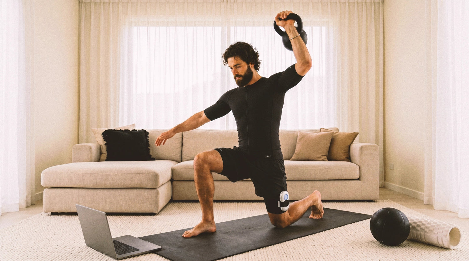 Man wearing EMS training suit performs a lunge on a living room mat with home workout accessories