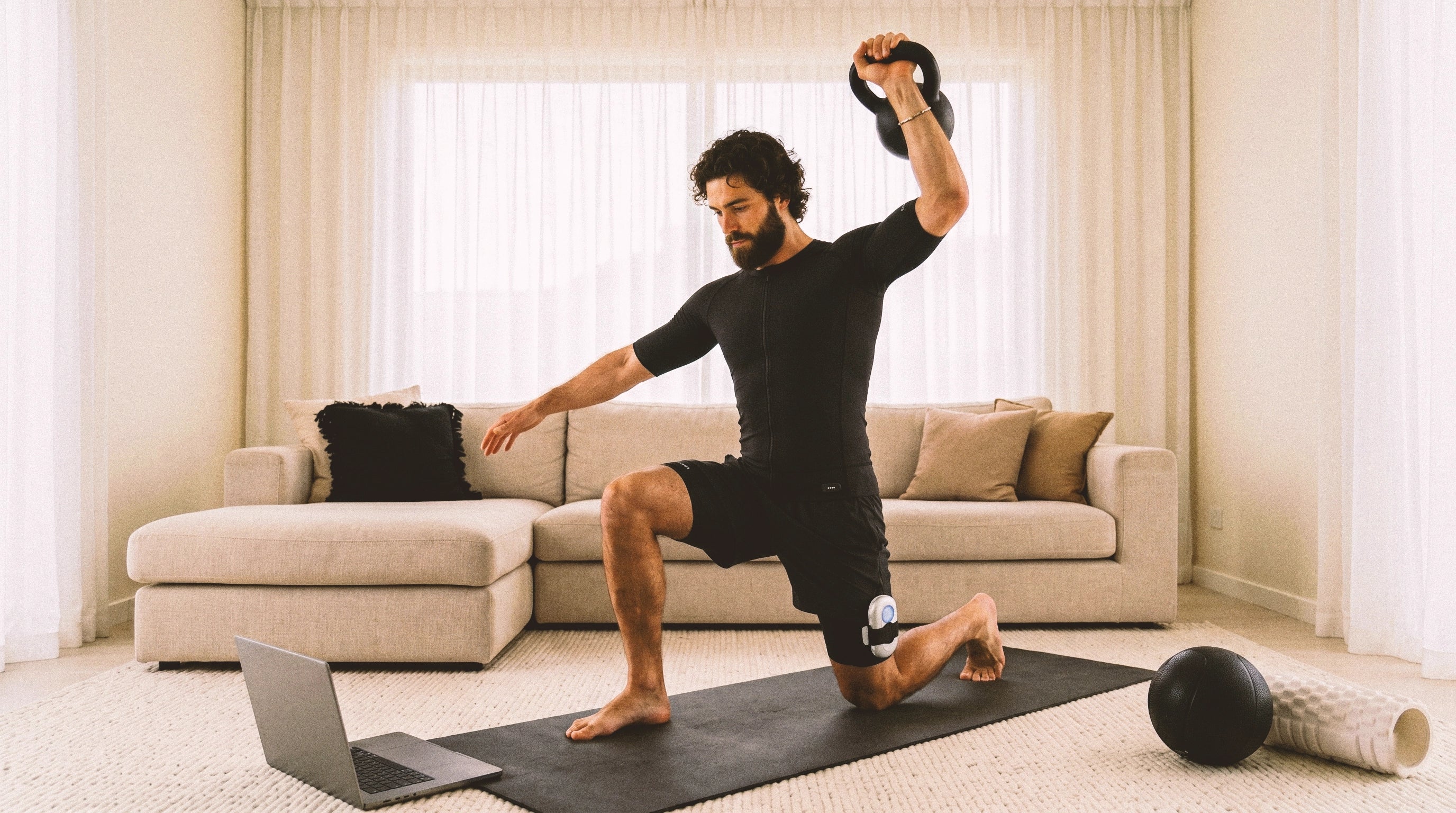 Man wearing EMS training suit performs a lunge on a living room mat with home workout accessories