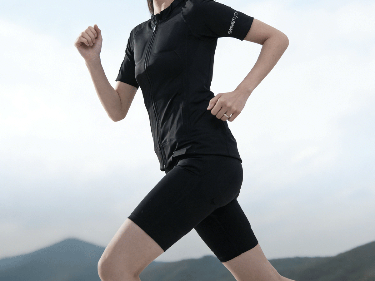 Close-up of a runner wearing a black SweetMyo training suit in motion against a soft outdoor landscape.