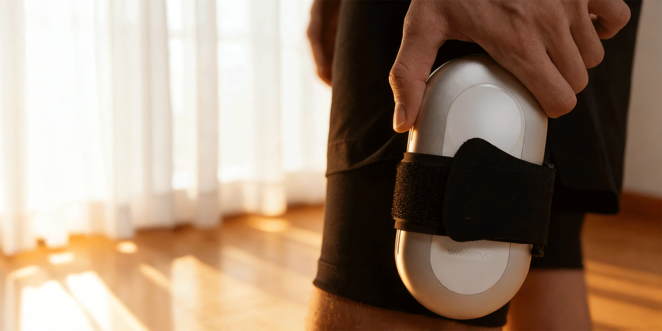 Close-up of a hand placing a SweetMyo controller into a thigh strap on black training shorts in warm indoor light.